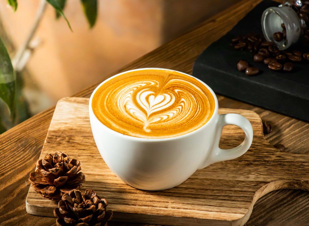Heart shaped latte art in a white cup with coffee beans